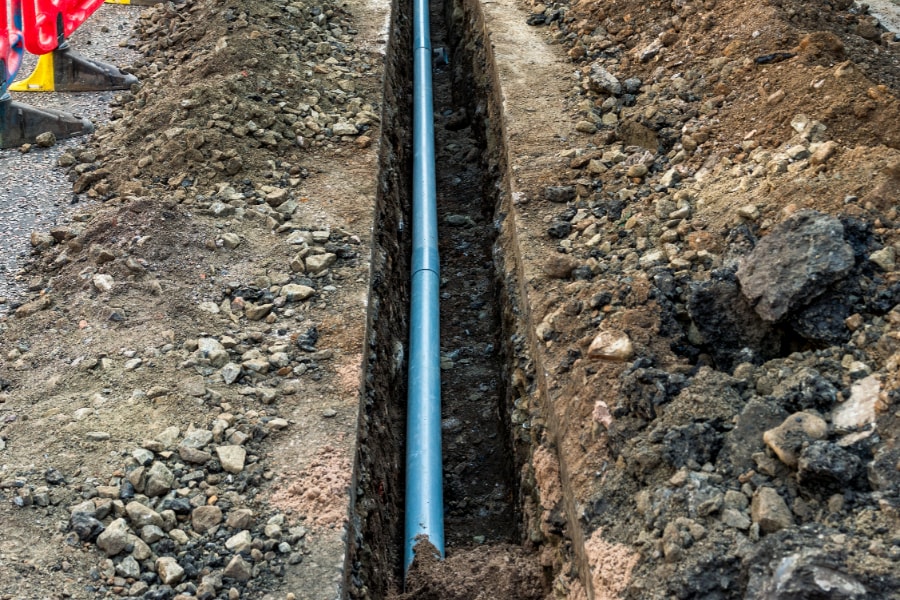 Blue surface water drainage pipe being laid in trench at roadside in Swansea by drainage Swansea contractors